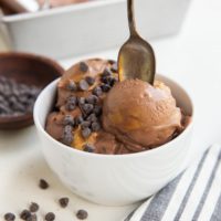 bowl of chocolate peanut butter ice cream with chocolate chips on top and a spoon ready to take a bite.