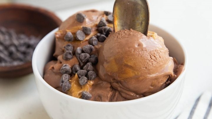 bowl of chocolate peanut butter ice cream with chocolate chips on top and a spoon ready to take a bite.