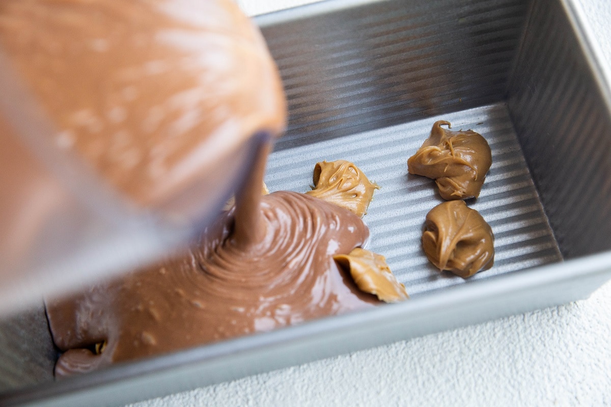 Pouring chocolate ice cream base over lumps of peanut butter into a freezer safe container