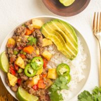 Bowl of Mexican Picadillo with rice and avocado. Limes, fork, and napkin off to the side.
