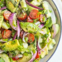 blue-rimmed bowl of avocado salad with a gold spoon to the side.