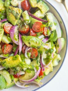 blue-rimmed bowl of avocado salad with a gold spoon to the side.