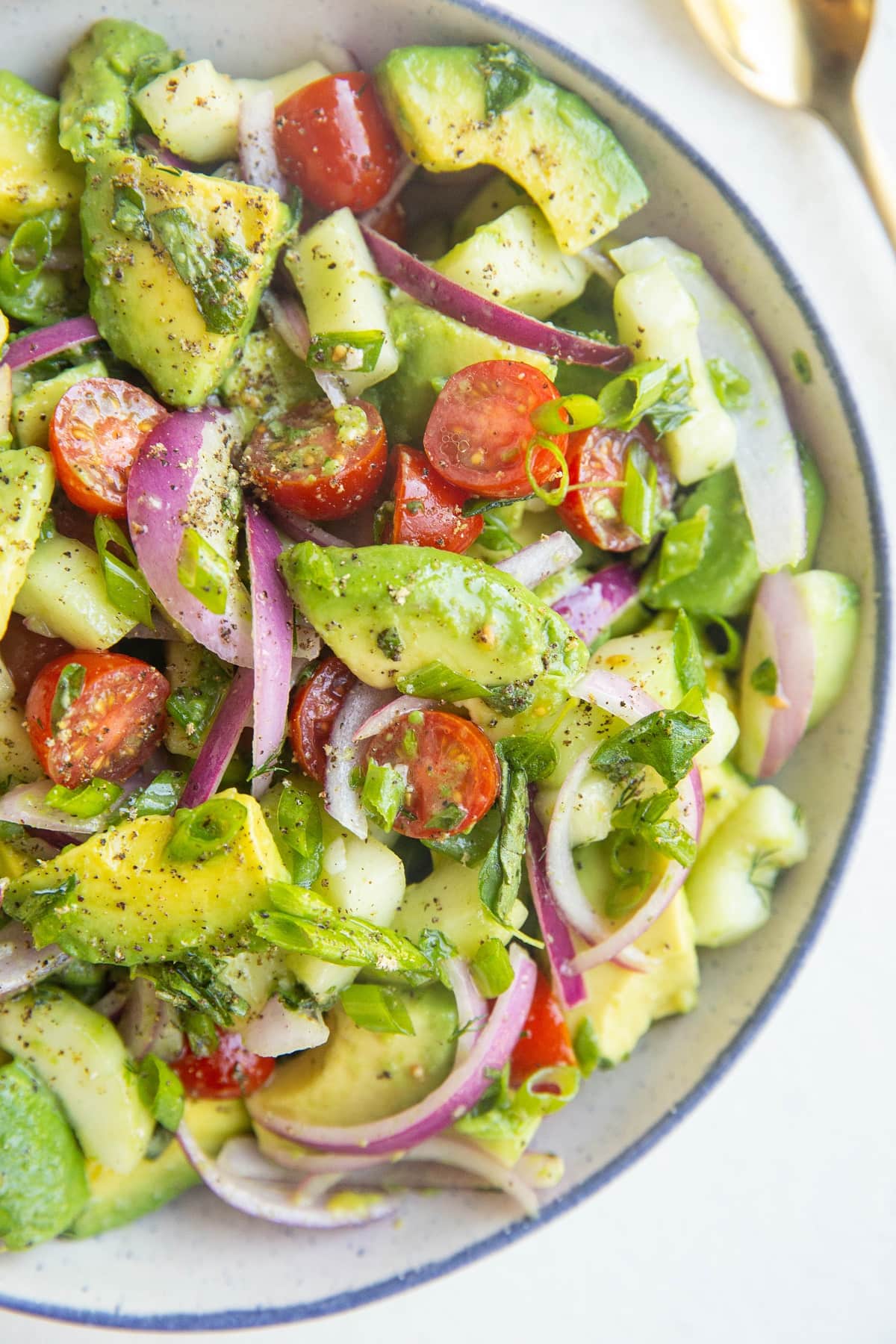 blue-rimmed bowl of avocado salad with a gold spoon to the side.