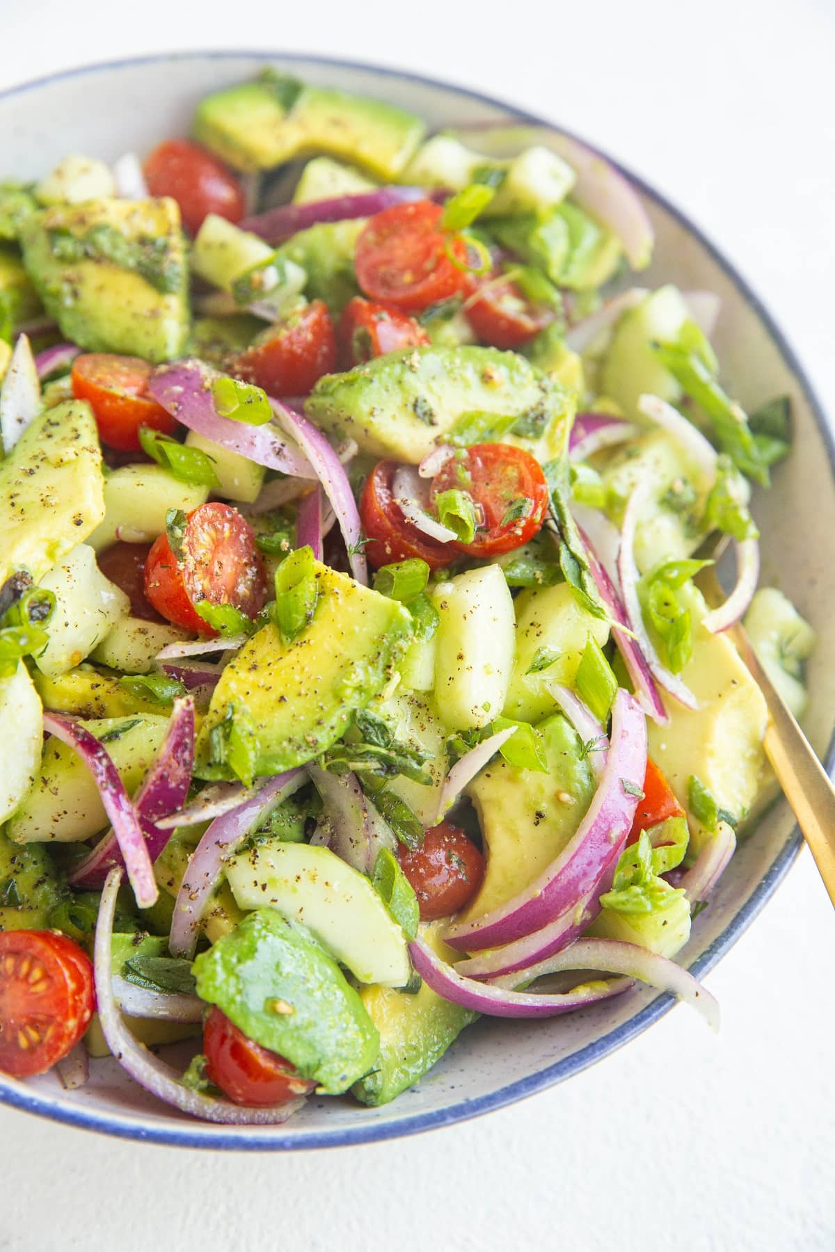 Avocado Salad in a blue-rimmed bowl with a gold spoon in it, ready to serve.