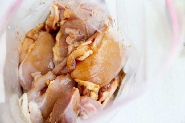 Raw chicken thighs in a zip lock bag with marinade just poured in.