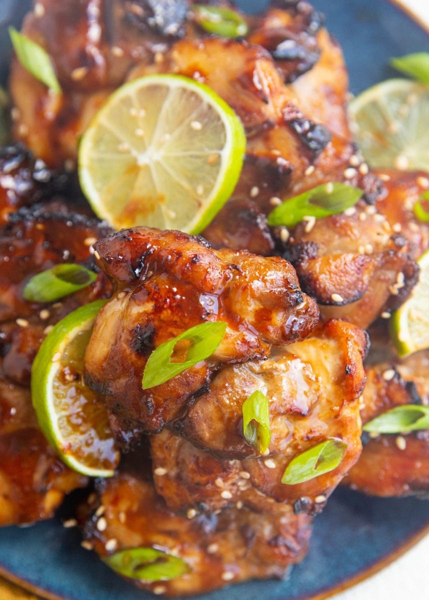 close up shot of a chicken thigh on a blue plate with more chicken thighs sprinkled with green onion