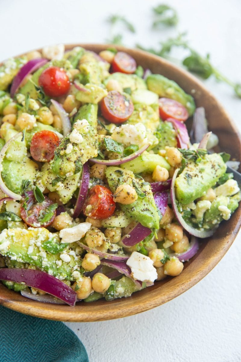 Close up image of chickpea avocado salad in a wooden bowl with a blue napkin