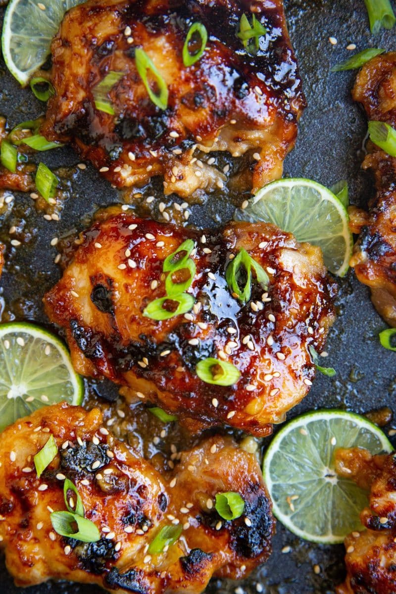 Casserole dish of honey lime chicken with slices of lime and chopped green onion on top.