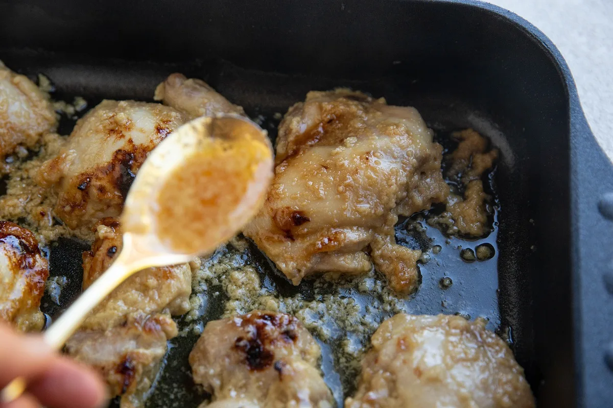 Basting the chicken thighs with juices from the pan