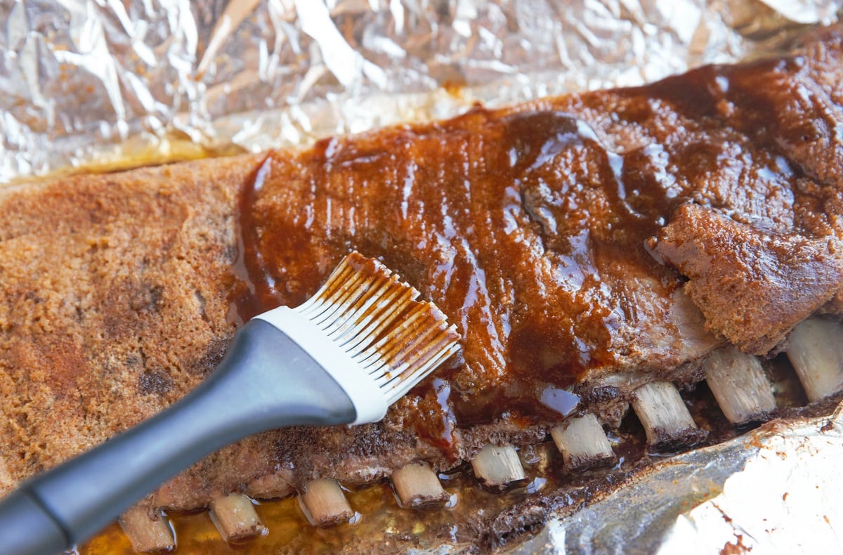 Baked ribs being brushed with barbecue sauce.