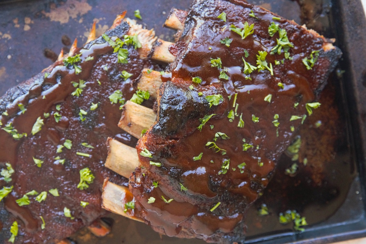 Horizontal image of rack of ribs on a baking sheet with barbecue sauce.