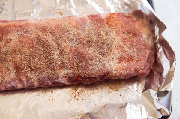 rack of ribs on a sheet of tin foil on a baking sheet rubbed with dry rub spices