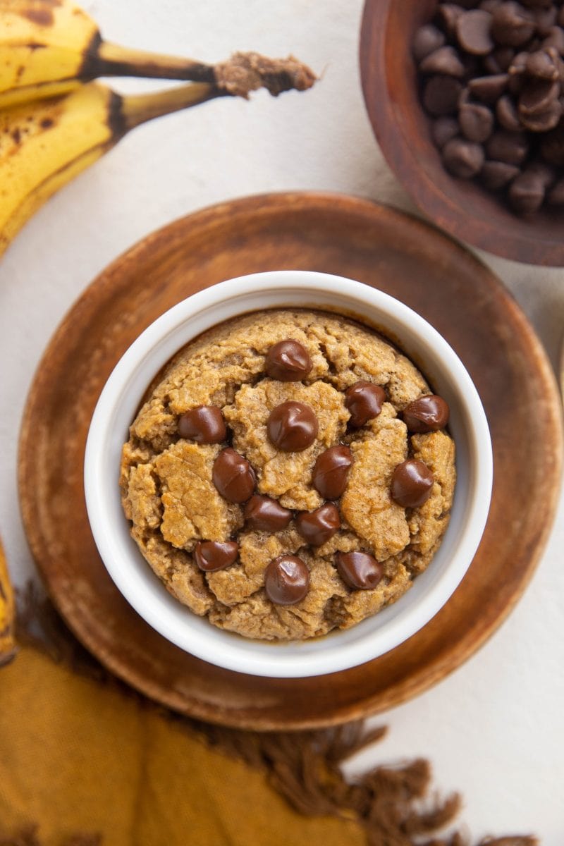 Top down shot of blended oats in a ramekin with chocolate chips on top, bananas to the side and a golden napkin