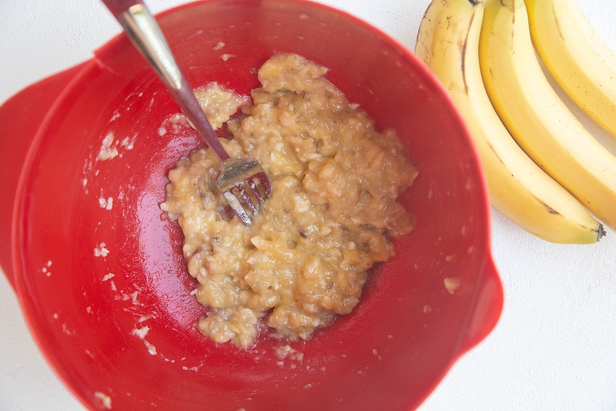 Mashed banana in a red mixing bowl.