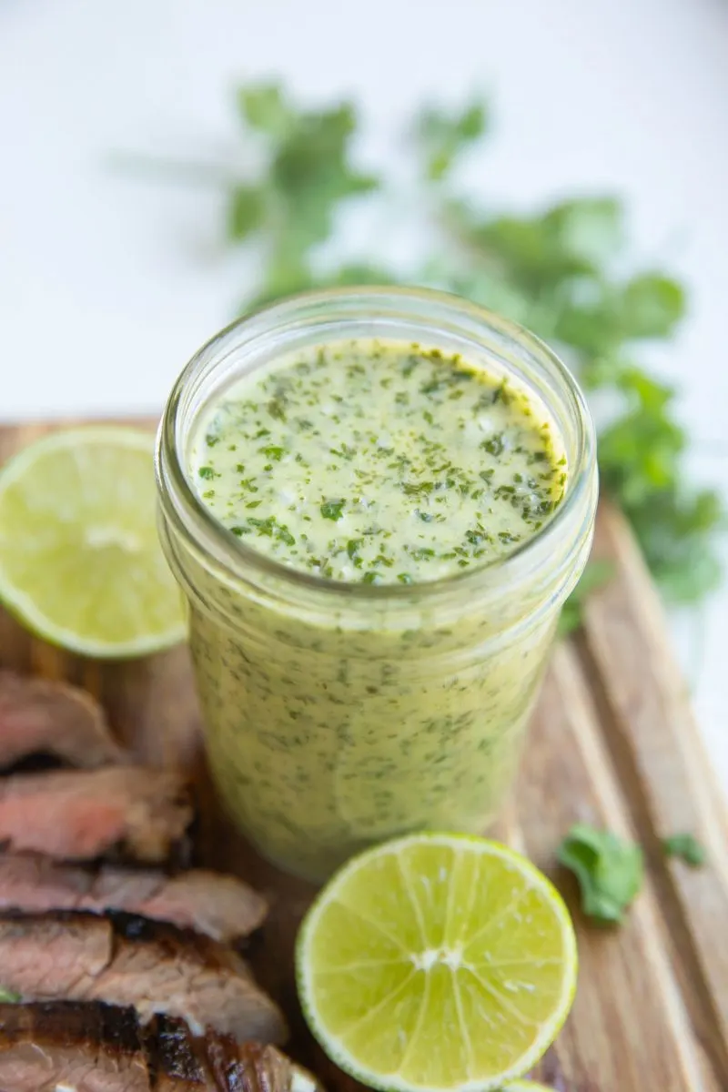 mason jar of blended chimichurri sauce with a sliced steak next to it