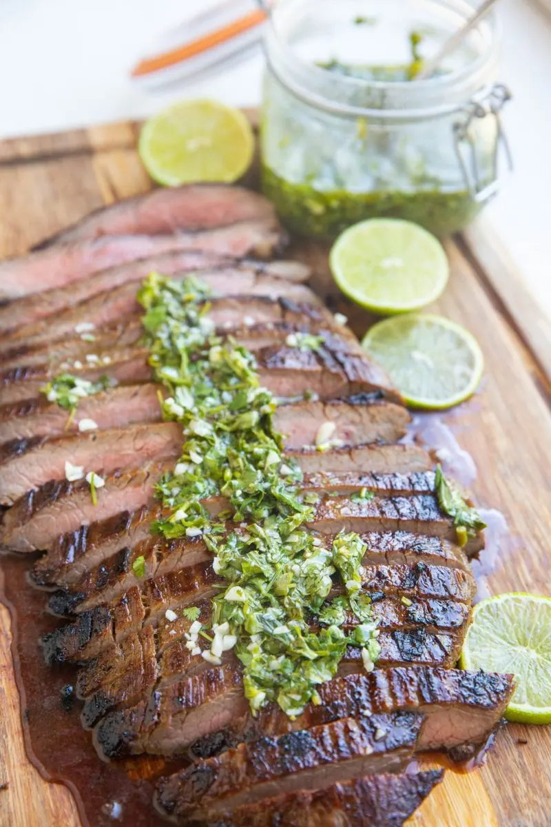 Skirt steak sliced on a cutting board with chimichurri sauce on top.