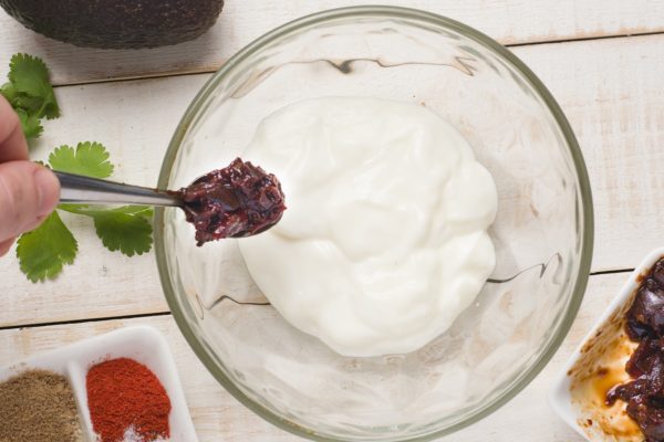 Bowl of greek yogurt with chipotle peppers being added to it