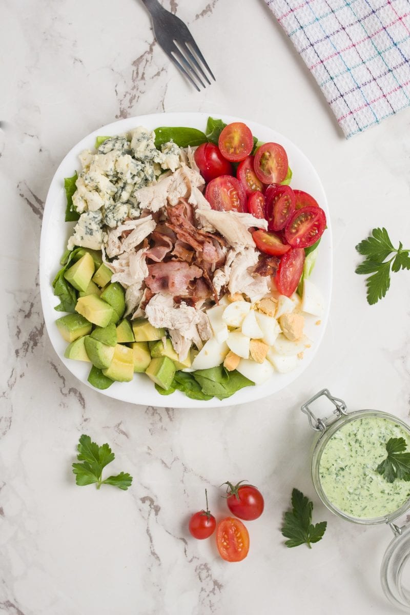 Top down photo of Cobb Salad on a white surface with a napkin and dressing to the side.