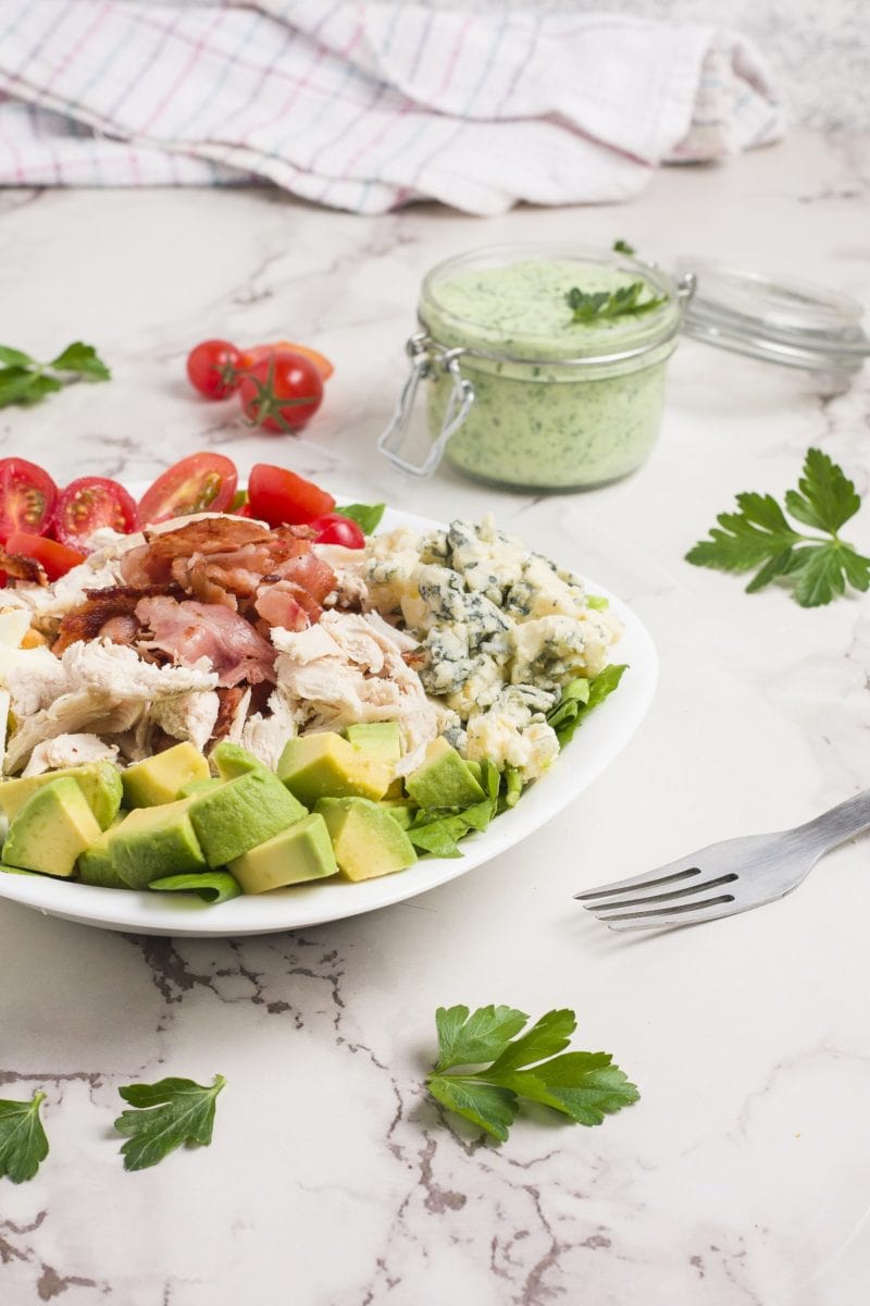 Bowl of salad on a marble surface with a jar of goddess dressing in the background.