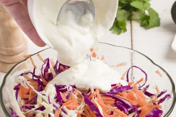 Ingredients for coleslaw in a bowl with yogurt being added to it.