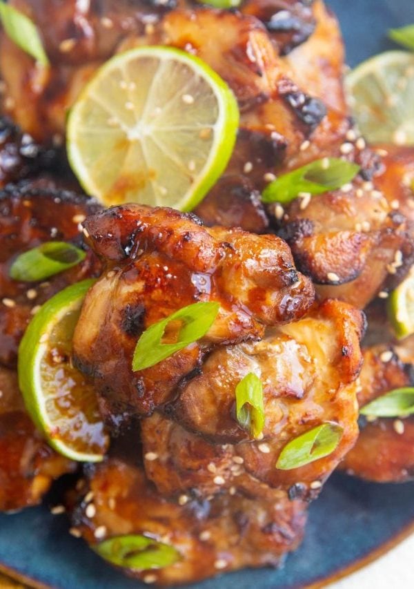 close up shot of a chicken thigh on a blue plate with more chicken thighs sprinkled with green onion