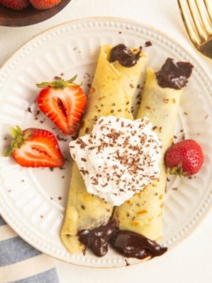 Plate of gluten-free crepes with chocolate filling, topped with whipped cream and berries.