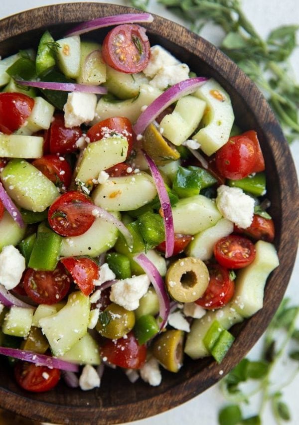 Wooden bowl of traditional Greek Salad with fresh herbs to the side.
