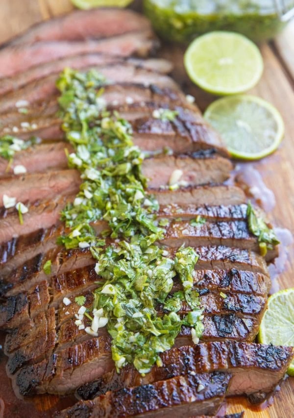Finished skirt steak on a cutting board sliced up drizzled with chimichurri sauce.