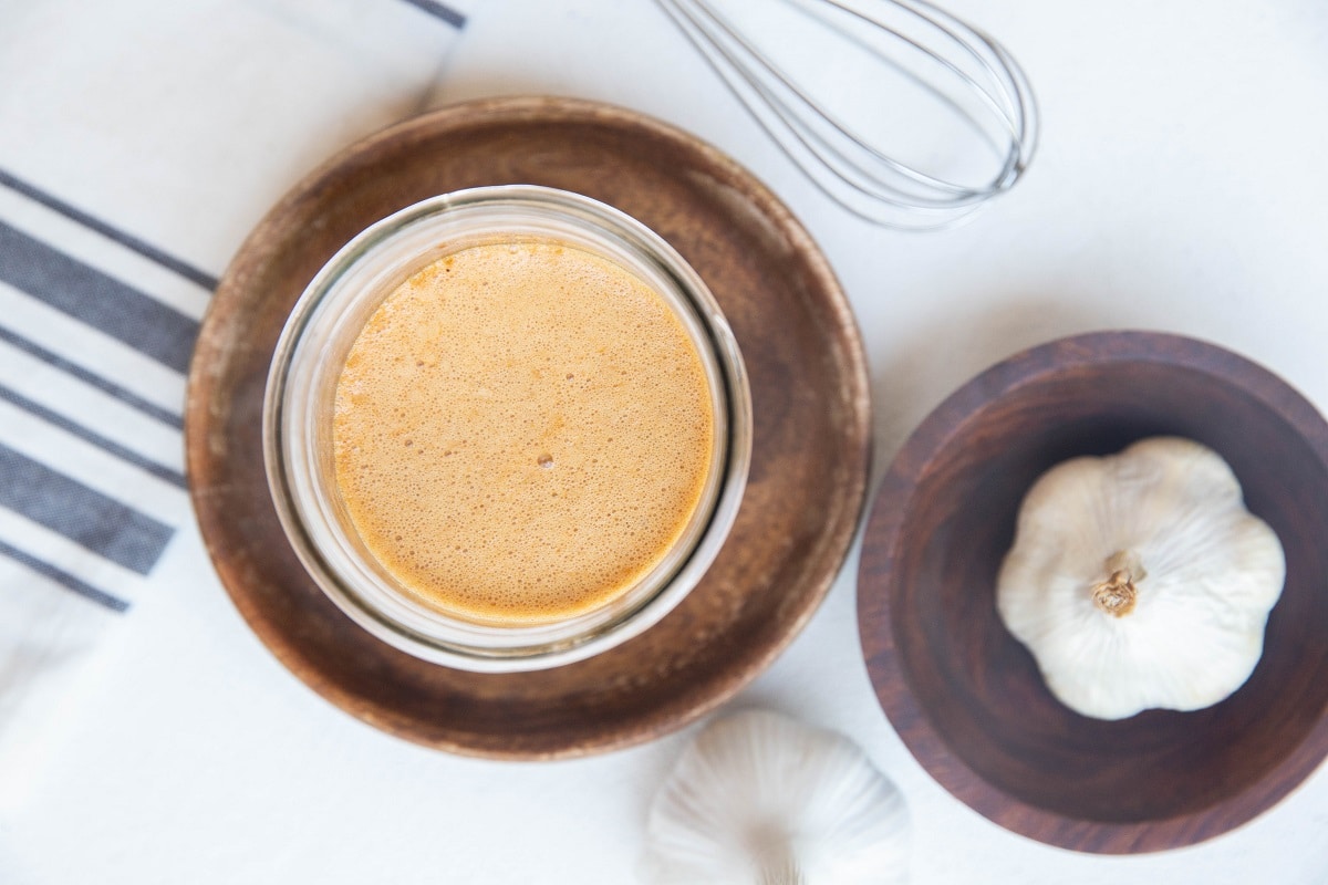 marinade in a jar with a napkin, garlic, and whisk to the side.