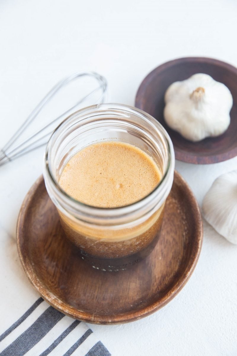 Flank steak marinade in a jar with garlic and a whisk to the side