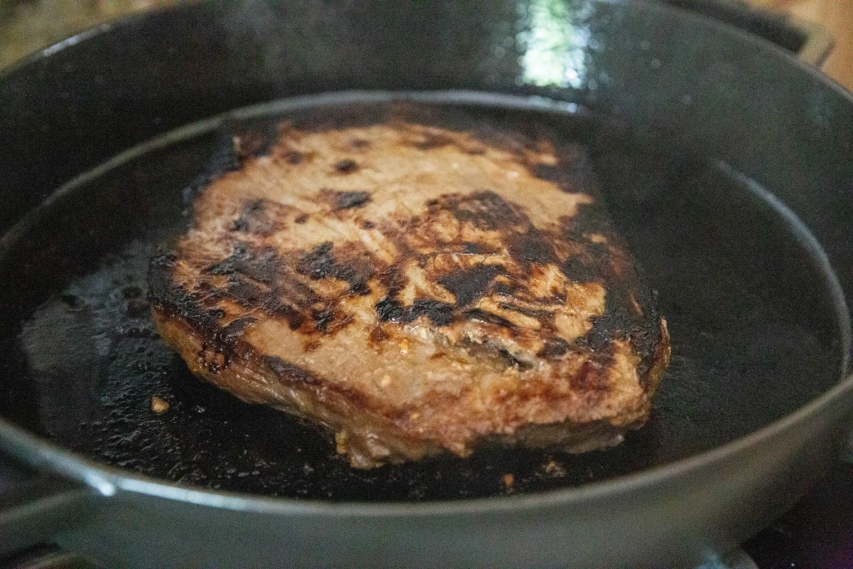 Flank steak cooking in a skillet