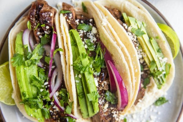 horizontal photo of flank steak tacos on a plate with red onion and avocado