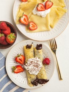 Two plates of crepes, one plate has chocolate filled crepes with strawberries.