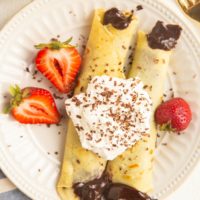 Plate of gluten-free crepes with chocolate filling, topped with whipped cream and berries.