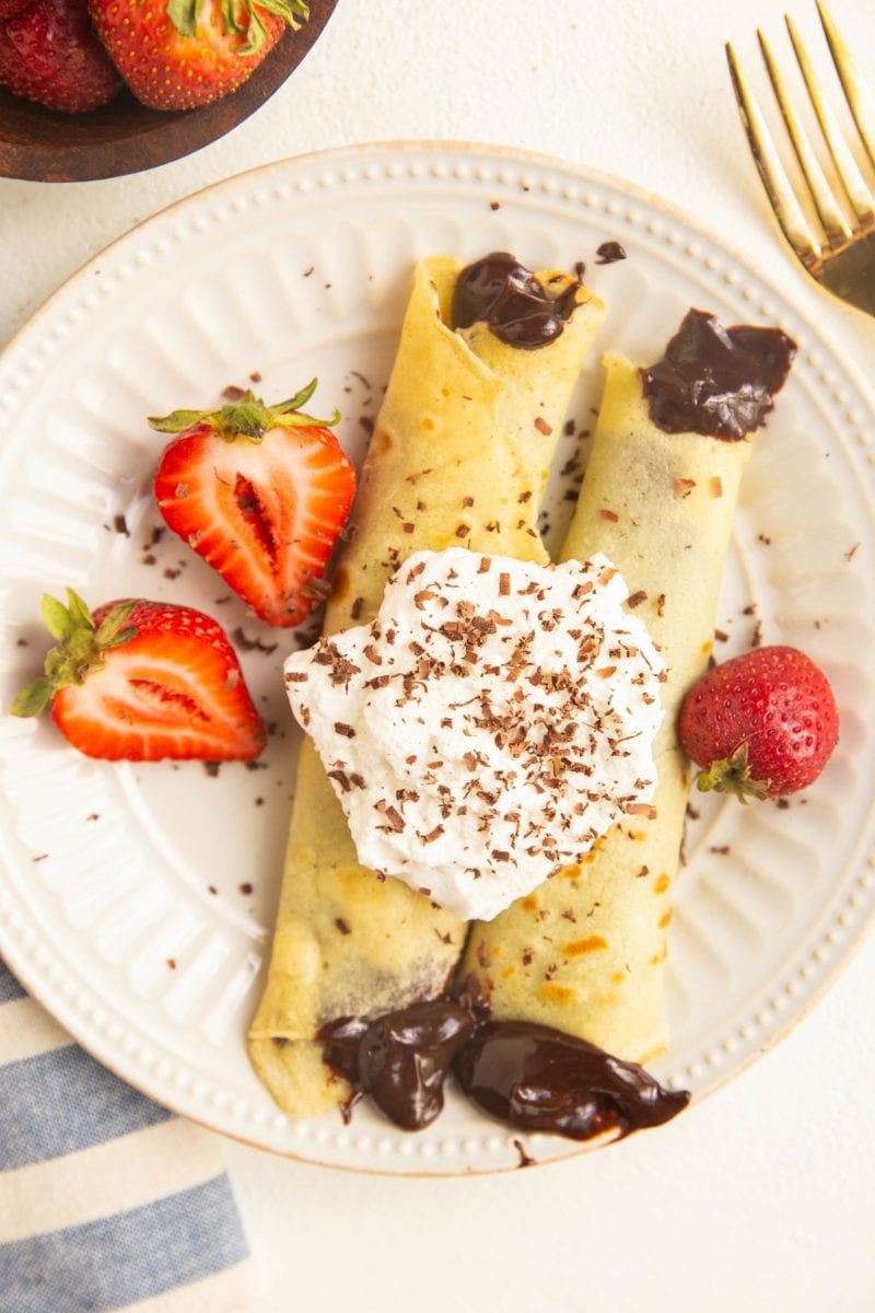Plate of gluten-free crepes with chocolate filling, topped with whipped cream and berries.
