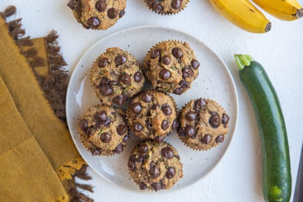 Horizontal top down photo of gluten-free zucchini muffins on a plate with a zucchini squash and bananas to the side.