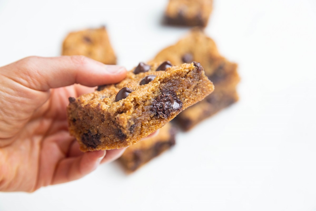 Hand holding one paleo pumpkin blondie with melted chocolate chips.