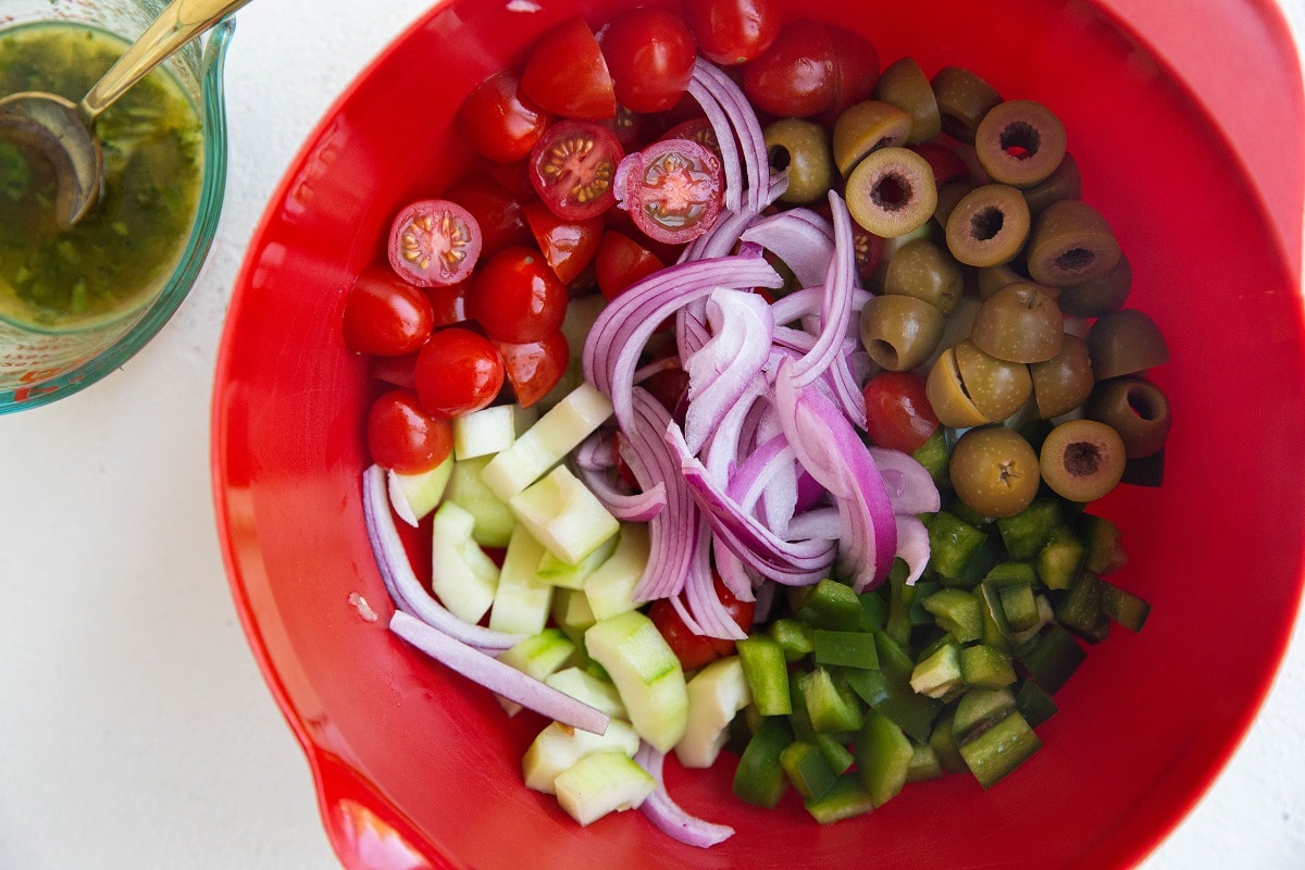 Greek salad ingredients in a large bowl with dressing in a small bowl to the side.