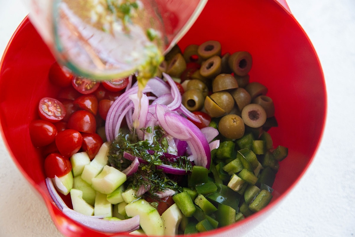 Pouring the Greek dressing into the bowl with the fresh salad ingredients.