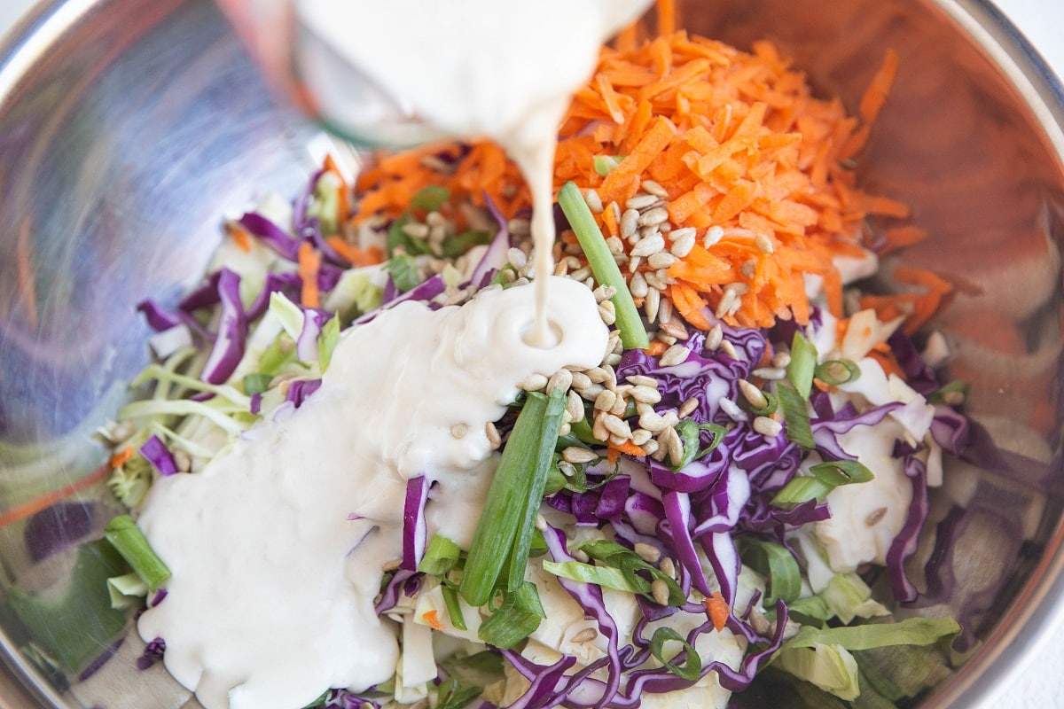 Pouring creamy yogurt dressing into the bowl with the veggies.