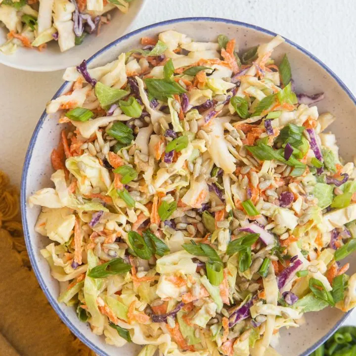Large bowl of healthy colelsaw and a small white bowl of coleslaw with a napkin and spoon to the side.
