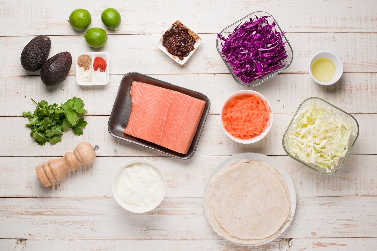Ingredients for salmon tacos on a white backdrop.