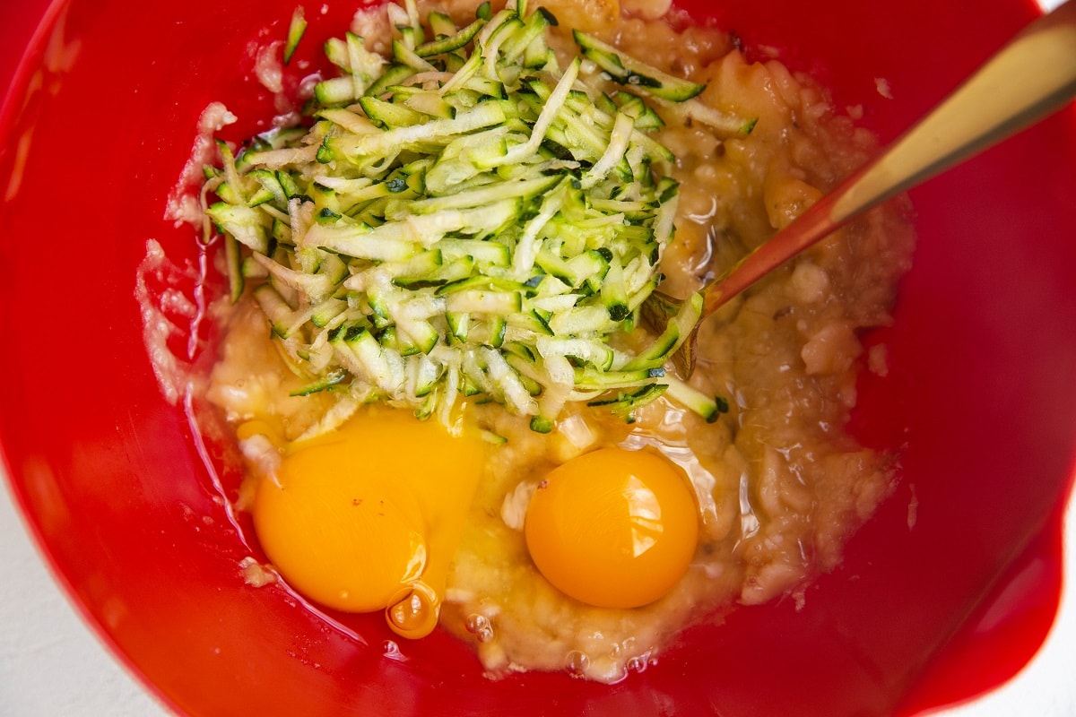 Mashed bananas, grated zucchini and eggs in a mixing bowl.