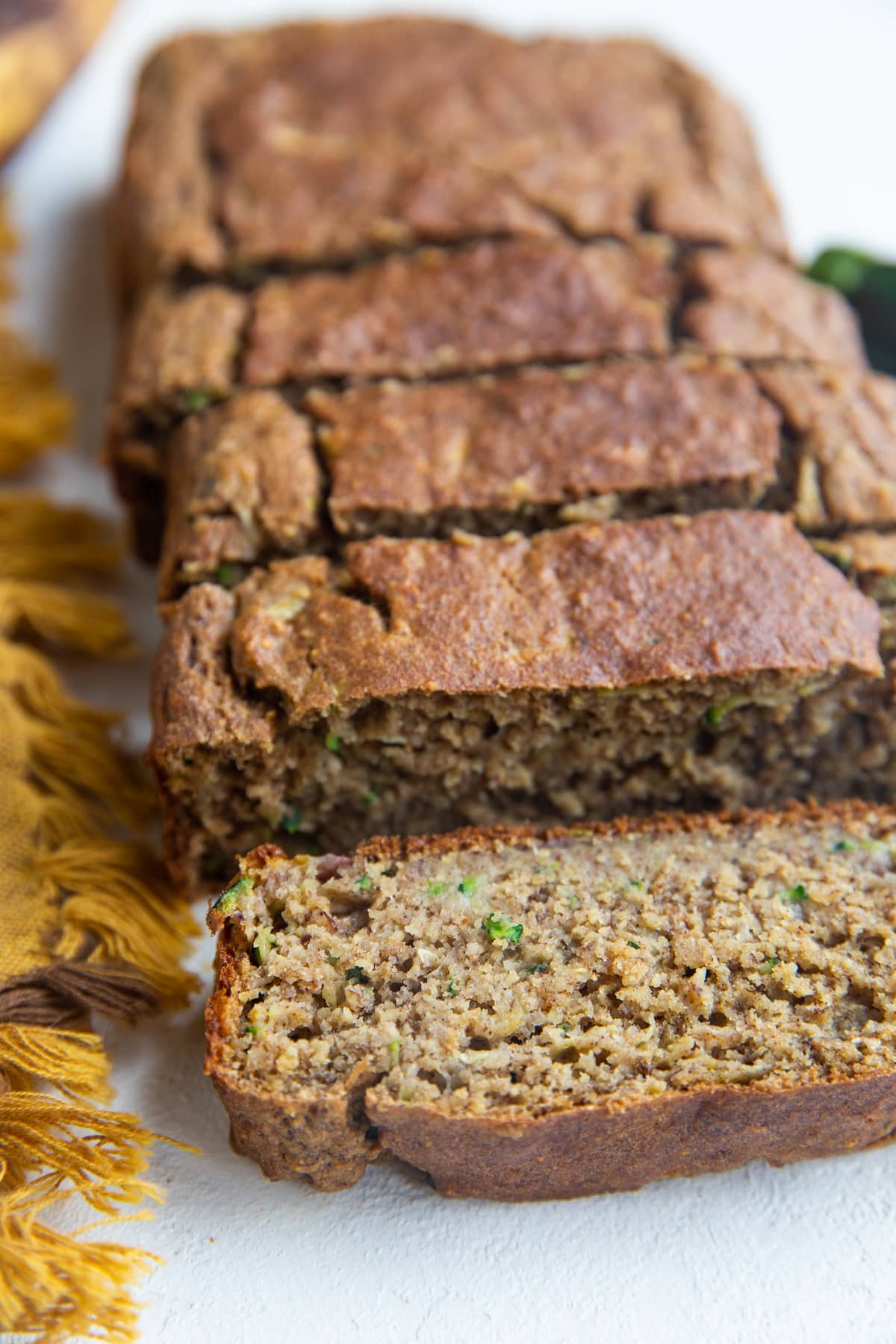 Loaf of zucchini banana bread on a white backdrop in slices.