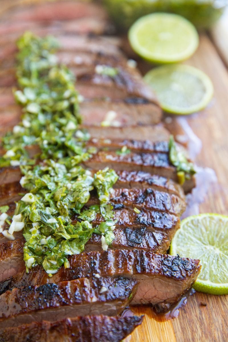 Cutting board with slices of skirt steak and chimichurri sauce on top.