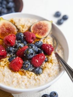 close up image of steel cut oatmeal in a bowl with fresh fruit and a spoon.