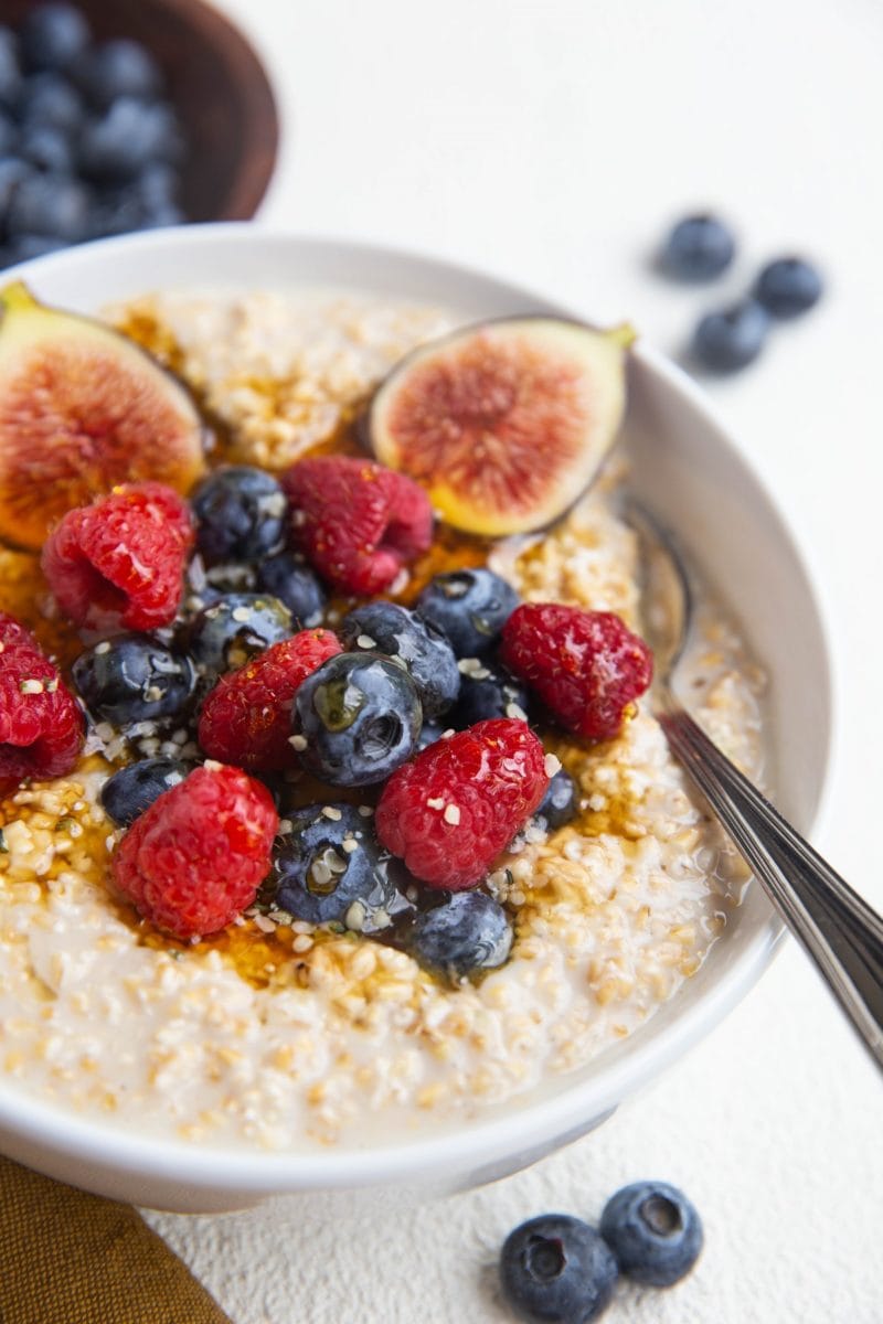 close up image of steel cut oatmeal in a bowl with fresh fruit and a spoon.