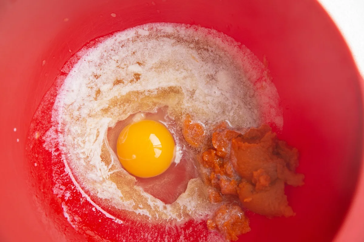 Red mixing bowl with pumpkin, melted butter, and an egg inside.