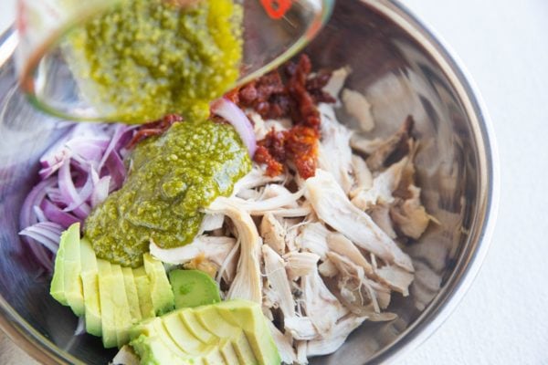 Pouring pesto sauce over the chicken salad ingredients.