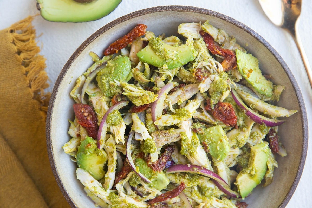 large serving bowl of chicken pesto salad with a golden napkin to the side and a gold spoon.